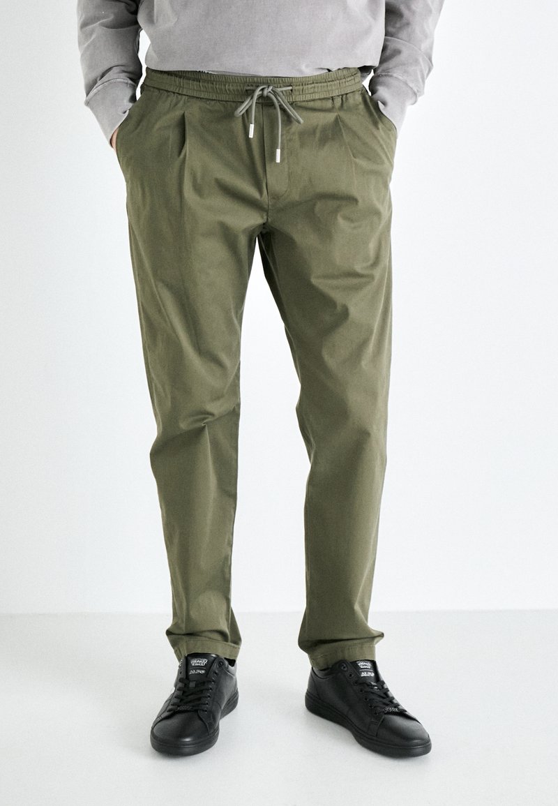 Pantalones livianos de color verde oliva con cintura elástica, cordón ajustable y bolsillos laterales; combinados con zapatillas negras.
