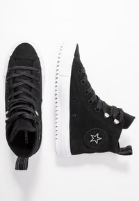 Schwarze Wildleder-Hochtop-Sneaker mit weißer Gummisohle, runder Zehenpartie, metallischen Ösen und Sternlogo an der Seite. Texturiertes Material mit Schnürsenkeln.
