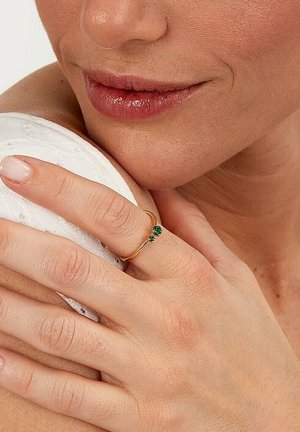 Goldring mit einem kleinen grünen Edelstein, der am Ringfinger getragen wird, mit einem dünnen Band und zartem Design, das von natürlichen Hauttönen ergänzt wird.