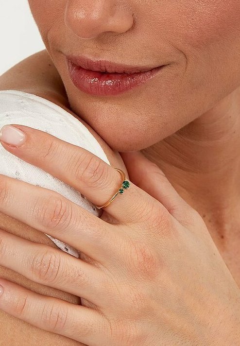 Guldring med en liten grön ädelsten, bärs på ringfingret, med en tunn band och en delikat design, kompletterad med naturliga hudtoner.