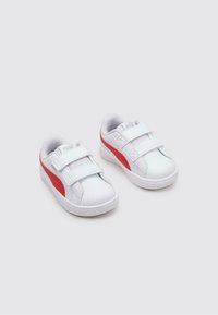 Sneakers bianchi con accenti rossi, realizzati in materiale sintetico. Presentano due cinturini in velcro, punta arrotondata e pannello laterale texturizzato.