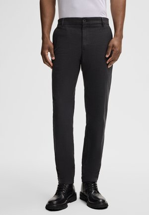 Black, fitted trousers in a textured fabric, featuring a button closure and side pockets, paired with black lace-up boots.