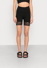 Sorte shorts med en tætsiddende design, prydet med spidsede kanter i blonder ved kanten. Kombineret med sorte sandaler med stropper. Glat tekstur hele vejen igennem.