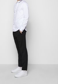 Vit bomullsskjorta med svart krage, matchad med svarta byxor och vita sneakers. Skjortan har långärmar och två knappar.