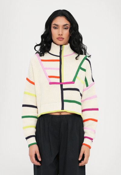 Pull en maille court crème avec des rayures multicolores (vert, rose, orange, marine) et un col haut avec une fermeture éclair à l'avant.