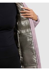 Gewatteerde jas met een lichtpaarse buitenkant en een metallic zilveren voering, met een doorgestikte textuur en een hand die op de opening rust.