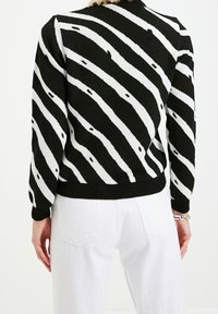 Musta-valkoraidallinen neulepaita, jossa on teksturoitu neulos, ribbineulos helmassa ja hihojen resoreissa. Takakuva näyttää rohkean kuosin ja istuvan mallin.