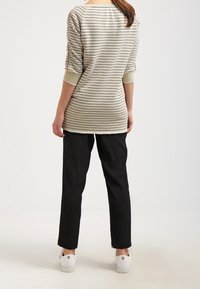 Maglietta a maniche lunghe a righe nei colori bianco sporco e taupe, con scollo a barca e dettagli testurizzati sui polsini, abbinata a pantaloni neri e sneakers bianche.