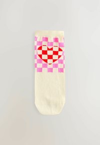 Krämfärgad strumpa med ett rutig mönster i rosa och vitt, med en röd hjärtdesign i centrum, mot en ljus bakgrund.