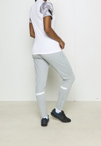 Sportliches Outfit mit einem weißen Shirt und gemusterten grauen Ärmeln, kombiniert mit grauen Hosen und schwarzen Sneakers mit blauen Akzenten.