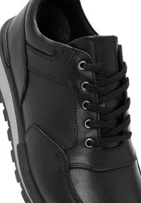 Sneaker in pelle nera con cinque occhielli in metallo e lacci neri, colletto imbottito e suola in gomma testurizzata visibile su sfondo bianco.