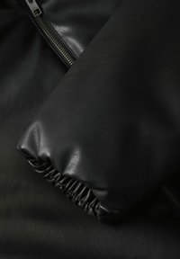 Czarna skórzana kurtka z dopasowanym mankietem z elastycznym marszczeniem. Gładka tekstura i metalowy zamek błyskawiczny wzdłuż jednej strony.