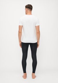 White short-sleeve t-shirt and black leggings on a male model, showcasing smooth fabric, fitted design, and a minimalistic style.