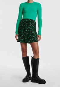 Maglietta verde a coste a maniche lunghe e una gonna nera con motivi floreali verdi, abbinata a stivali neri al ginocchio con una finitura testurizzata.