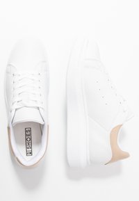 Bílé kožené tenisky s kulatou špičkou a plochou podrážkou. Texturovaný béžový akcent na patě, šest průhledů pro tkaničky a perforované detaily.