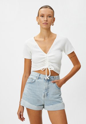 Vit ribbad crop top med djup V-ringning och samlat frontdetalj. Matchas med ljusblå denimshorts med uppvikta ärmar.
