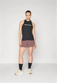 Svart ermeløs tanktopp med hvit logo, kombinert med burgunder shorts. Modellen har på seg lyse treningssko og svarte sokker.