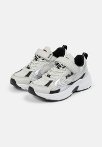 Baskets de sport blanches en mesh avec des accents noirs et argentés, avec une sangle Velcro, des lacets, et une semelle blanche épaisse.