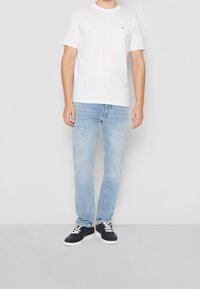 T-shirt bianca a maniche corte con scollatura rotonda; jeans in denim azzurro chiaro; sneaker blu navy con accenti e lacci bianchi.