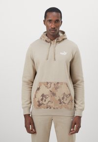 Sudadera beige hecha de una mezcla de algodón con un bolsillo frontal de camuflaje tonal. Cuenta con capucha ajustable y logo bordado en el pecho.