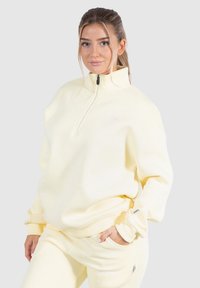 Gul zip-up sweatshirt i mjukt tyg med ribbade ärmar. Har en hög krage och subtil logotyp framtill.