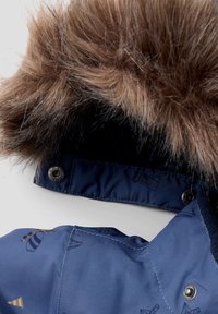 Chaqueta azul marino con capucha forrada de piel, tejido brillante con patrones sutiles y broches a presión en el cuello.