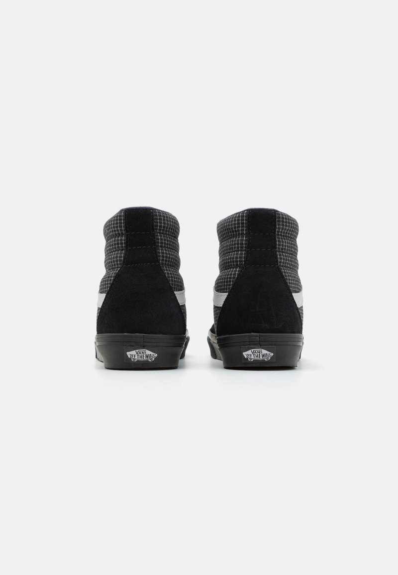 Un paio di sneakers alte Vans nere e grigie viste da dietro, con il logo "Off The Wall" sul tallone, su uno sfondo bianco.