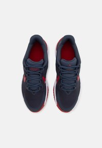 Baskets de sport pour homme avec une tige en maille bleu foncé, accents rouges, surface texturée, lacets plats, col rembourré et semelle blanche durable.