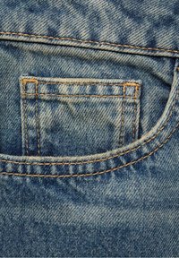 Tessuto in denim blu con una tasca posteriore con cuciture visibili. La texture è liscia con un leggero motivo sbiadito e un piccolo segno di usura.