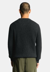 Suéter de color gris oscuro con textura que presenta un diseño acanalado con un patrón de punto trenzado que recorre la parte trasera. Mangas largas y cuello redondo.