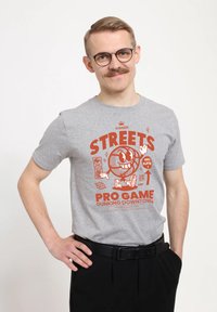 Šedé bavlněné tričko s červeným grafickým potiskem, na kterém je usmívající se postava basketbalisty, text zní "STREETS PRO GAME DUNKING DOWNTOWN."