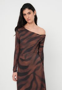 Κατασκευασμένο φόρεμα σε καφέ απόχρωση με μαύρο μοτίβο ρίγες τίγρης, με μακριά μανίκια και ασύμμετρο ντεκολτέ που αφήνει τον ώμο ακάλυπτο.