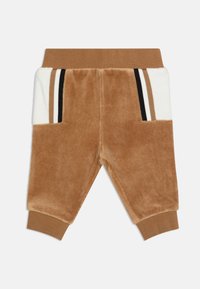 Pantaloni in velluto marrone per bambini con tasche laterali, accenti bianchi e strisce nere e marroni. Vita elasticizzata e polsini a costine. Texture morbida.