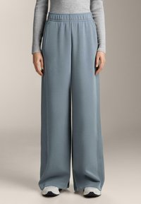 Svetlomodré široké tepláky s elastickým pásom a bočnými vreckami, vyrobené z mäkkej látky, skombinované s bielymi a námorníckymi teniskami.