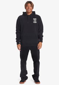 Black hoodie with front pocket, drawstring hood, and white graphic print on left side. Paired with black corduroy pants and black shoes.
