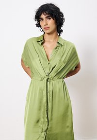 Hellgrünes Satin-Kleid mit Knopfverschluss vorne, kurzen Ärmeln, Bindegurt in der Taille und fließender Silhouette.