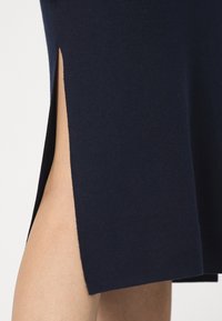 Abito blu navy con uno spacco laterale, realizzato in un tessuto morbido. La texture appare liscia e l'orlo è rifinito in modo impeccabile, rivelando la pelle sottostante.