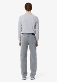 Chemise grise à manches longues et jean gris ample. Le jean a des poches arrière et une étiquette à la taille. Les chaussures sont des baskets blanches.