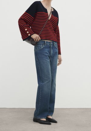 Personne portant un pull rayé noir et rouge avec des boutons dorés, un jean droit taille haute bleu, des ballerines noires et un petit sac bandoulière marron.