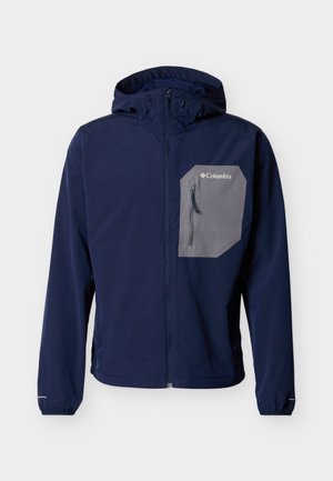 Veste à capuche bleu marine avec fermeture éclair complète à l'avant et poche poitrine zippée grise arborant le logo Columbia sur fond blanc.