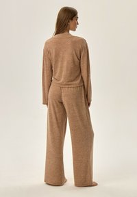 Jasnobrązowy zestaw odzieży wypoczynkowej składający się z luźno dopasowanej bluzki z długim rękawem i spodni z szerokimi nogawkami, wykonany z miękkiego materiału o teksturowanym wykończeniu.