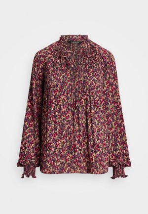 Blouse à manches longues florale avec poignets smockés, col haut à volants, plis devant et petit lien au cou dans des tons rouges, roses et beiges.