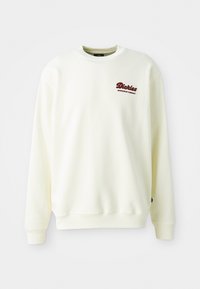 Cream-colored sweatshirt made of soft fabric, featuring a round neckline and ribbed cuffs. Displays a maroon logo on the left chest.