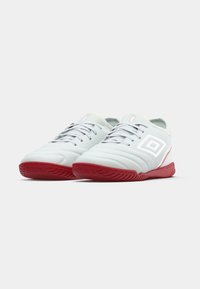 Zapatillas deportivas blancas con una parte superior texturizada, suela de goma roja y acentos rojos; presenta un logo de diamante en el costado y diseño de cordones.
