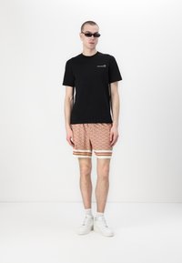 Czarna bawełniana koszulka z białym napisem, wzorzyste pomarańczowe szorty z białymi i czerwonymi paskami oraz białe trampki. Akcesorium: małe czarne okulary przeciwsłoneczne.