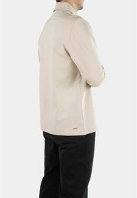 Camicia beige a maniche lunghe con colletto a risvolto, realizzata in cotone, con un piccolo logo arancione vicino all'orlo e una vestibilità rilassata.