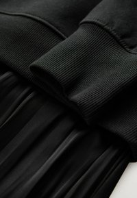Black sweatshirt material with ribbed cuffs above a black pleated fabric, creating a layered look with contrasting textures.
