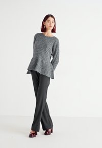 Siv pulover iz pletene tkanine z rebrasto teksturo in peplum obliko, v kombinaciji s črnimi krojenimi hlačami. Manekenka nosi bordeaux rjav škornje na peto. Bela podlaga.
