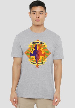 Young man wearing a gray t-shirt with a colorful "Weasleys' Wizard Wheezes" logo featuring two stylized wizards and stars.