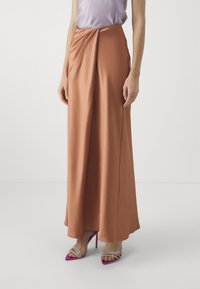 Gonna lunga in tessuto arancione bruciato con un design morbido e drappeggiato. Abbinata a sandali con tacco alto rosa e una maglietta di un leggero viola.